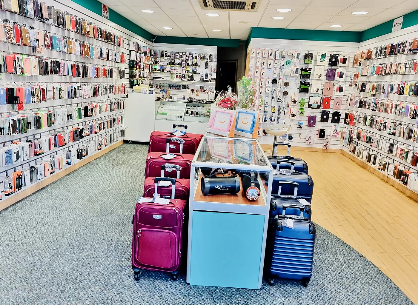 De winkel van binnen: wanden vol hoesjes onder de groene rand, koffers en een vitrine